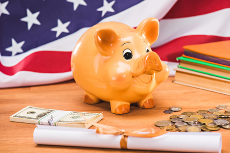 diploma and piggy bank with coins and dollars usa flag behind (cost of tuition)