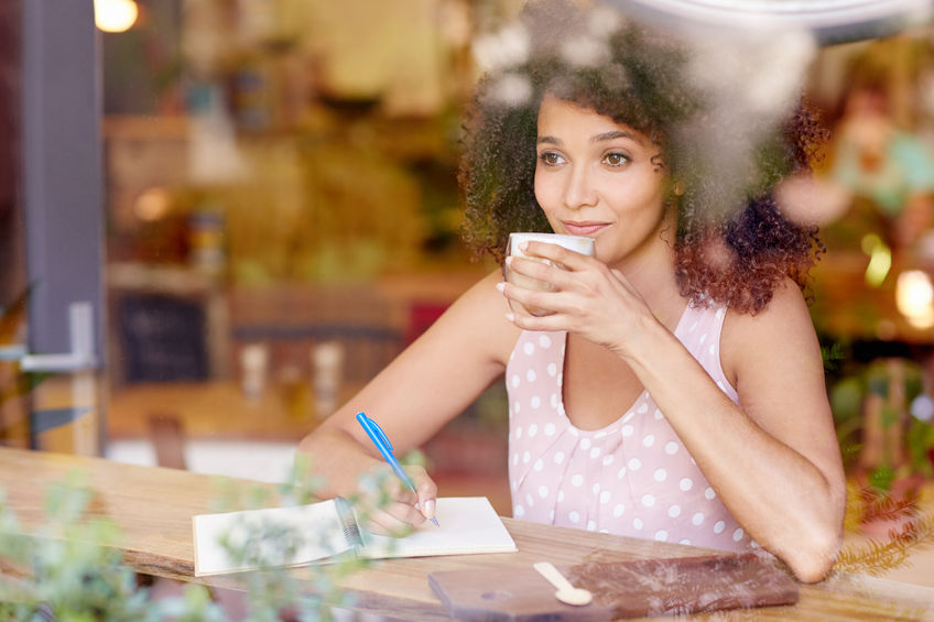 beautiful mixed race woman sitting in a coffee shop sipping her latte and daydreaming while gazing out of the window concept for How to End a Scholarship Essay